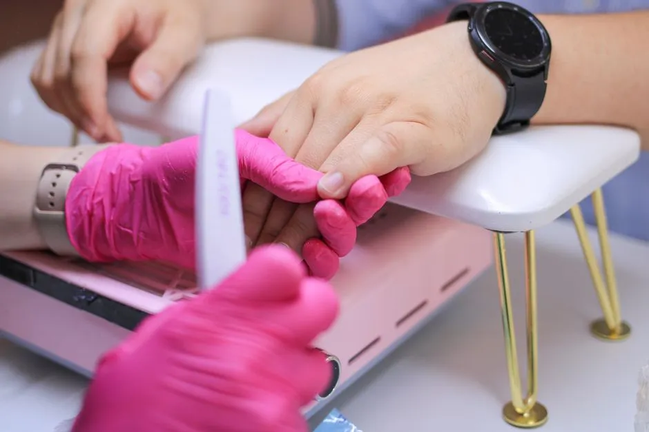 Händer med rosa handskar under nagelvård, exempel på hudskydd mot nagellim