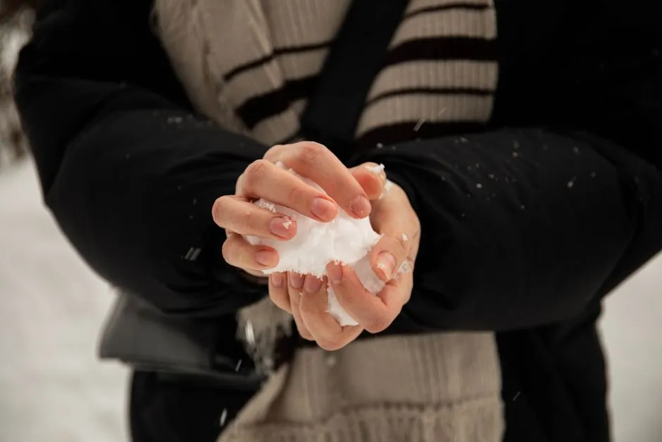Vinternaglar på bara händer som håller en snöboll utomhus i kyla